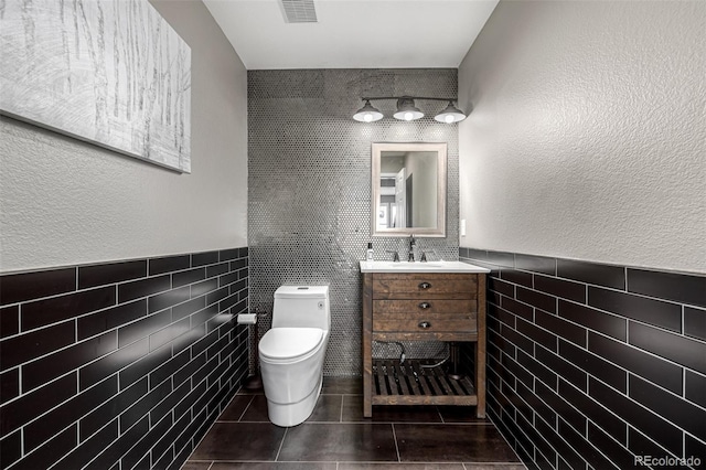 bathroom with visible vents, toilet, tile patterned flooring, vanity, and tile walls