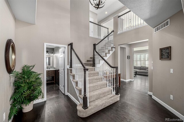 staircase featuring visible vents, a high ceiling, baseboards, and wood finished floors