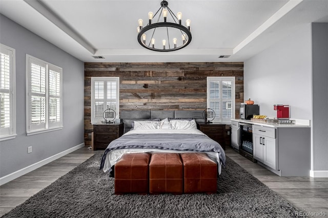 bedroom featuring beverage cooler, baseboards, an accent wall, a tray ceiling, and wood walls