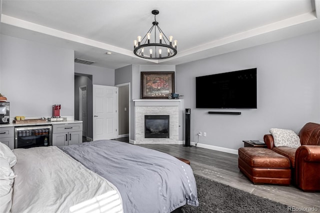 bedroom with baseboards, wine cooler, wood finished floors, a stone fireplace, and a notable chandelier