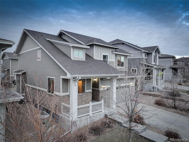 view of front of home with brick siding, roof with shingles, a porch, concrete driveway, and board and batten siding