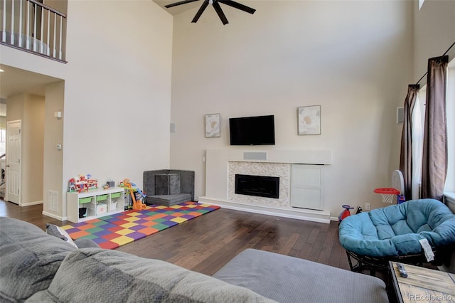 living room featuring baseboards, ceiling fan, hardwood / wood-style floors, a high ceiling, and a fireplace