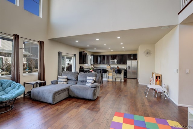 living area featuring baseboards, dark wood finished floors, a towering ceiling, and recessed lighting