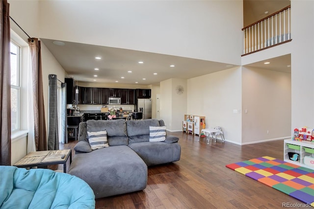 living area with a high ceiling, baseboards, dark wood finished floors, and recessed lighting