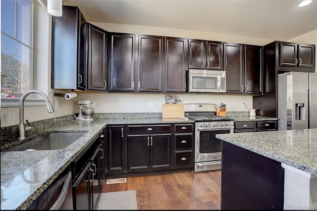 kitchen featuring dark wood finished floors, visible vents, appliances with stainless steel finishes, a sink, and light stone countertops