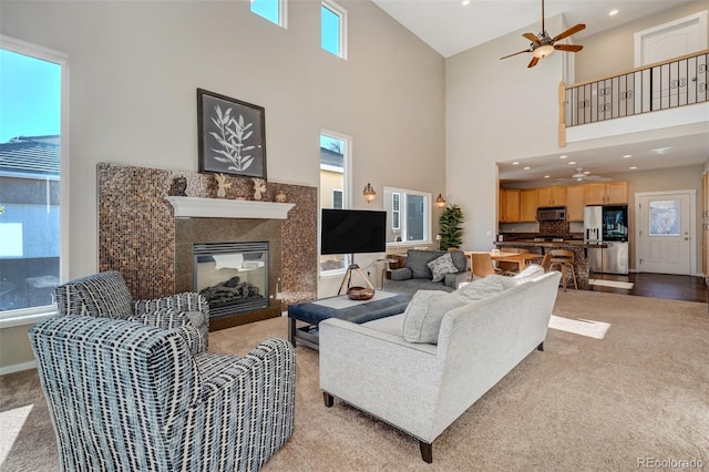 carpeted living room featuring a high ceiling, ceiling fan, and a premium fireplace