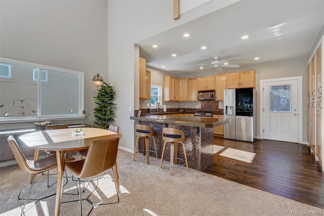 kitchen with kitchen peninsula, appliances with stainless steel finishes, backsplash, light brown cabinetry, and ceiling fan