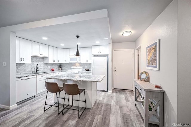 kitchen featuring hanging light fixtures, white cabinets, white appliances, a kitchen island, and light wood-type flooring