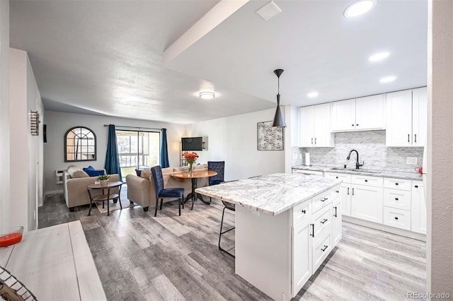 kitchen with white cabinetry, a kitchen island, hanging light fixtures, and light hardwood / wood-style floors