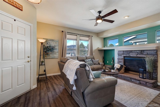 living room featuring dark wood-type flooring, a stone fireplace, and ceiling fan