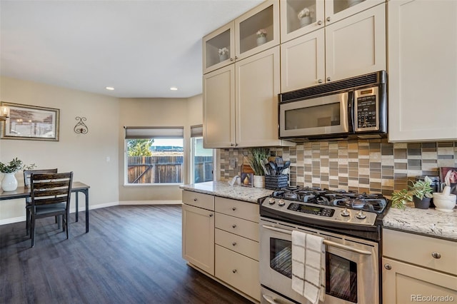 kitchen featuring appliances with stainless steel finishes, dark hardwood / wood-style flooring, backsplash, light stone counters, and cream cabinetry