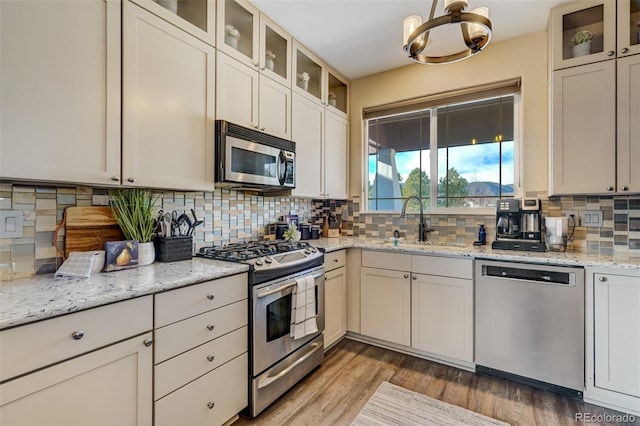 kitchen with hardwood / wood-style flooring, stainless steel appliances, tasteful backsplash, light stone countertops, and sink