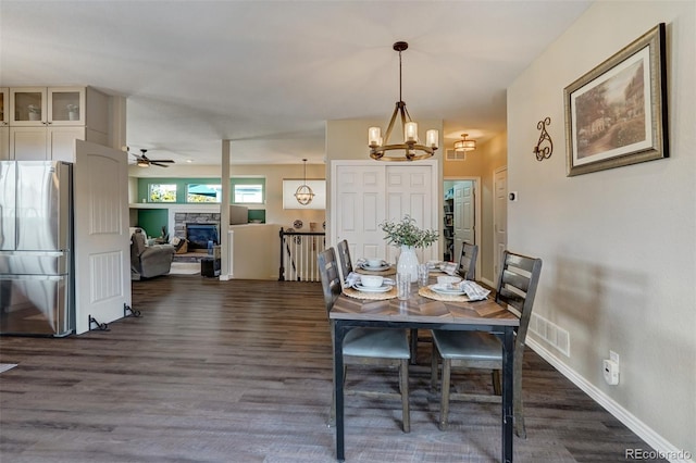 dining area featuring ceiling fan with notable chandelier, dark hardwood / wood-style floors, and a stone fireplace