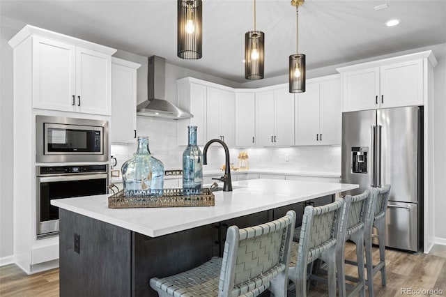 624 Simmental Loop, Castle Rock, CO 80104 - kitchen with appliances with stainless steel finishes, wall chimney exhaust hood, light wood-style flooring, an island with sink, and decorative backsplash