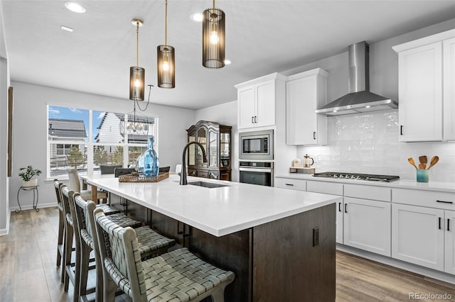 624 Simmental Loop, Castle Rock, CO 80104 - kitchen featuring wall chimney exhaust hood, stainless steel appliances, decorative backsplash, a kitchen island with sink, and white cabinetry