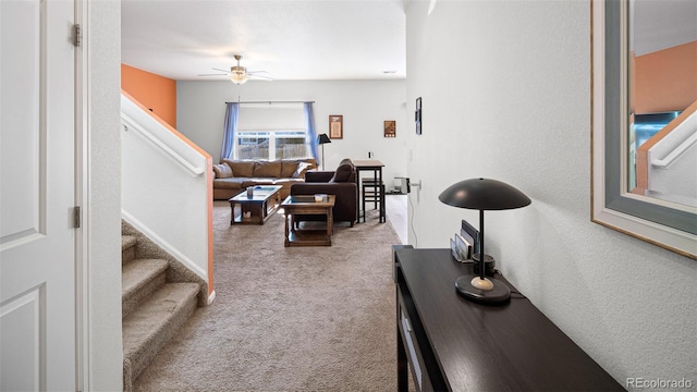 carpeted living area featuring stairs and ceiling fan