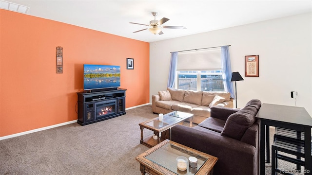 carpeted living room featuring ceiling fan, visible vents, baseboards, and a lit fireplace