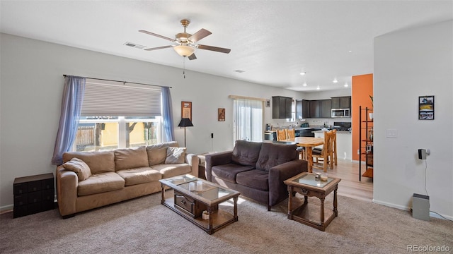 living area with a ceiling fan, visible vents, a wealth of natural light, and light carpet