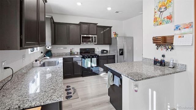 kitchen featuring dark brown cabinets, light stone counters, appliances with stainless steel finishes, light wood-style floors, and a sink