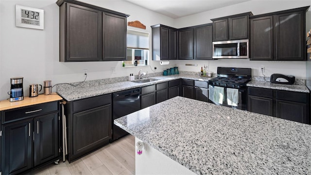 kitchen with light stone counters, black appliances, light wood-type flooring, and a sink