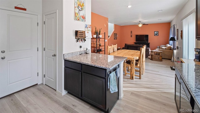 kitchen with light stone counters, dark cabinets, ceiling fan, light wood-style floors, and open floor plan