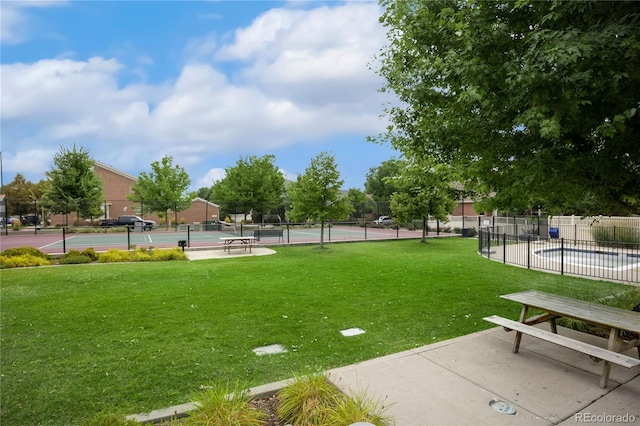 view of home's community with a tennis court, a lawn, and fence