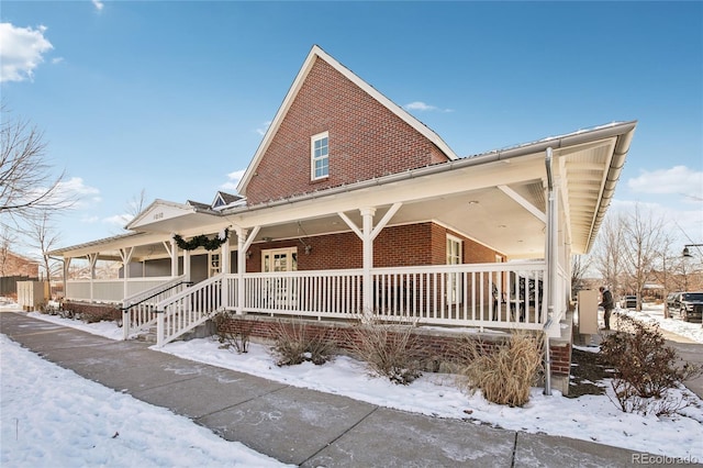 view of snowy exterior with a porch and brick siding