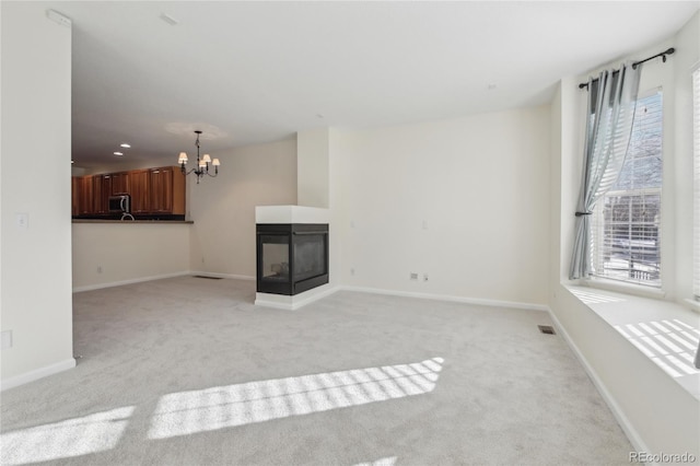 unfurnished living room with a chandelier, light carpet, a multi sided fireplace, and visible vents