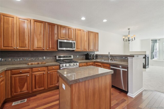 kitchen with visible vents, appliances with stainless steel finishes, a sink, wood finished floors, and a peninsula