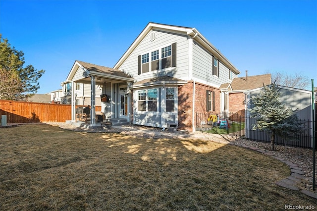 rear view of house with brick siding, a lawn, and fence