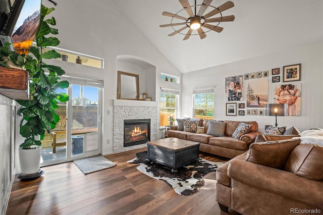 living room featuring high vaulted ceiling, a stone fireplace, hardwood / wood-style flooring, and a healthy amount of sunlight