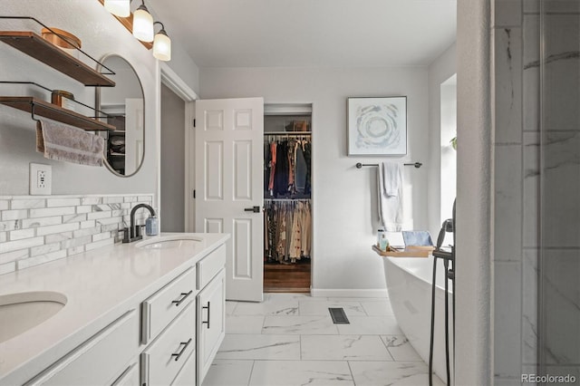 full bathroom with marble finish floor, double vanity, a freestanding bath, a spacious closet, and a sink