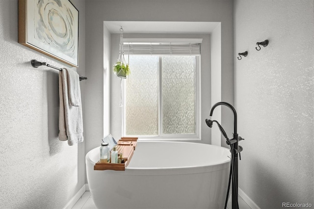 full bath with a textured wall, tile patterned flooring, a freestanding bath, and baseboards