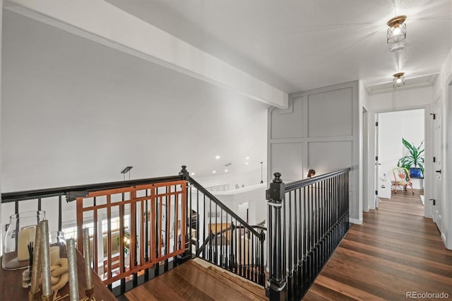 corridor featuring beam ceiling, wood finished floors, and an upstairs landing