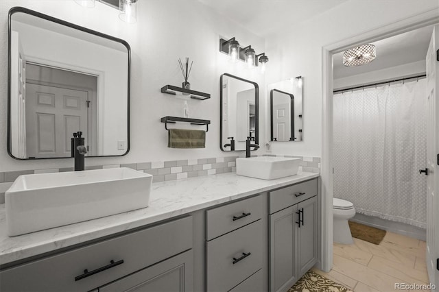 full bath with marble finish floor, a sink, toilet, and double vanity