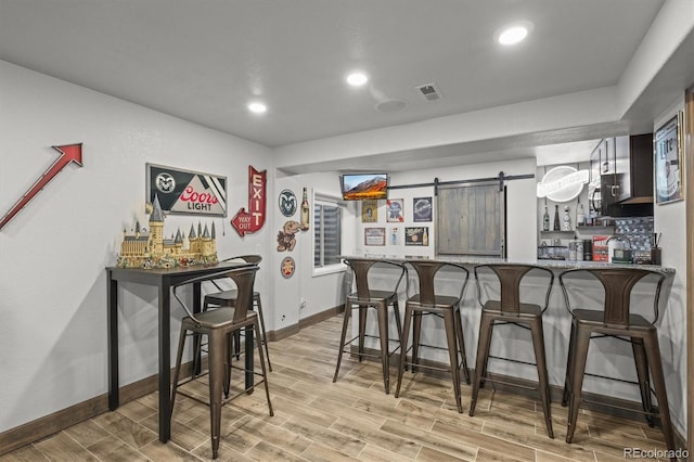 bar with a dry bar, a barn door, visible vents, wood tiled floor, and recessed lighting