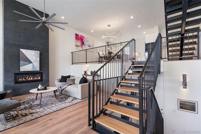 stairs with a high ceiling, a large fireplace, recessed lighting, a ceiling fan, and wood finished floors