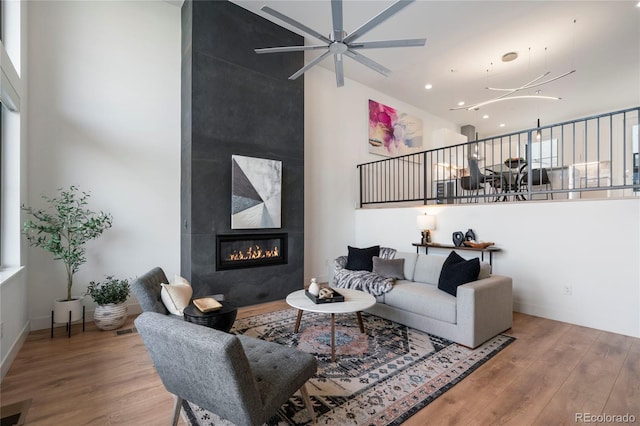 living room featuring a high ceiling, a tiled fireplace, a ceiling fan, recessed lighting, and wood finished floors