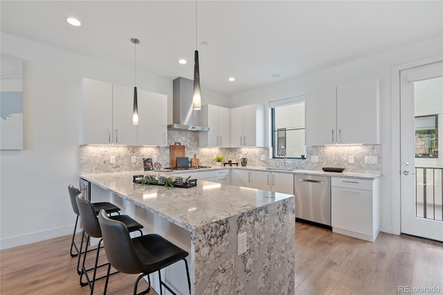 kitchen featuring light wood-style flooring, appliances with stainless steel finishes, wall chimney range hood, and a kitchen breakfast bar