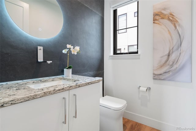 half bath with toilet, baseboards, wood finished floors, and vanity