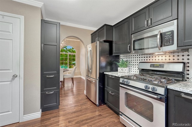 123 Wheat Ridge St, Palmer Lake, CO 80133 - kitchen with stainless steel appliances, ornamental molding, arched walkways, wood finished floors, and dark cabinets