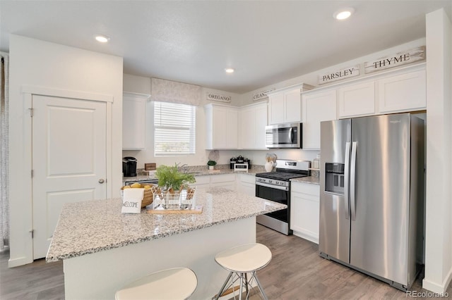 kitchen featuring light stone countertops, stainless steel appliances, a center island, and white cabinets