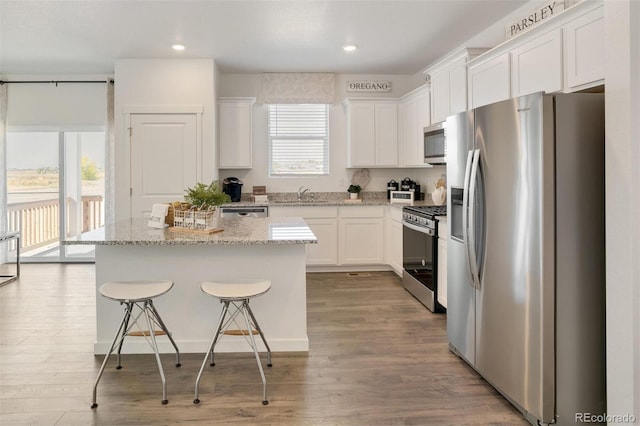 kitchen with light hardwood / wood-style flooring, appliances with stainless steel finishes, white cabinetry, a center island, and light stone counters