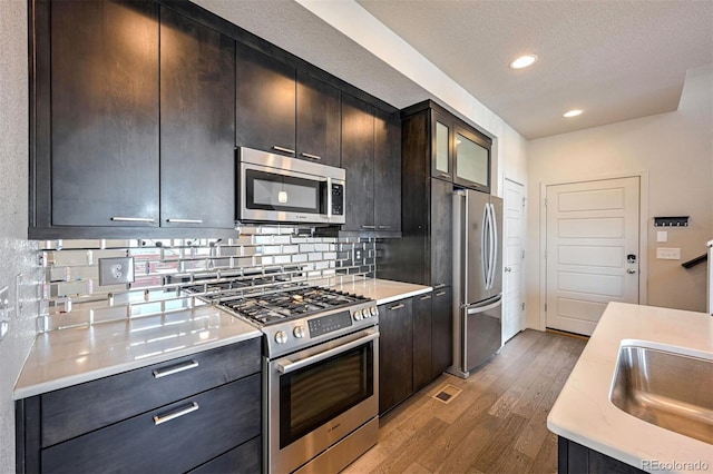 kitchen featuring hardwood / wood-style floors, appliances with stainless steel finishes, a textured ceiling, sink, and backsplash