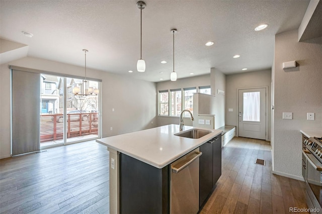 kitchen with stainless steel appliances, sink, hanging light fixtures, light wood-type flooring, and a center island with sink