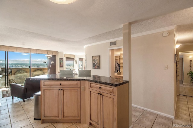 kitchen with a textured ceiling, dark stone counters, crown molding, and light tile patterned floors