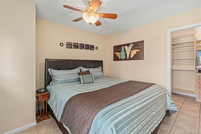 tiled bedroom with ceiling fan, a textured ceiling, a closet, and a walk in closet