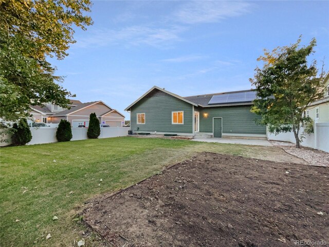 back of house featuring a lawn, a patio area, and solar panels