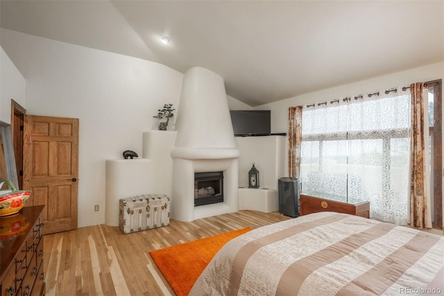 bedroom featuring a large fireplace, vaulted ceiling, and light wood-style flooring