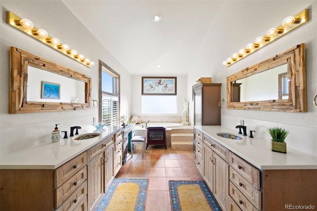 full bath featuring a garden tub, lofted ceiling, two vanities, and a sink